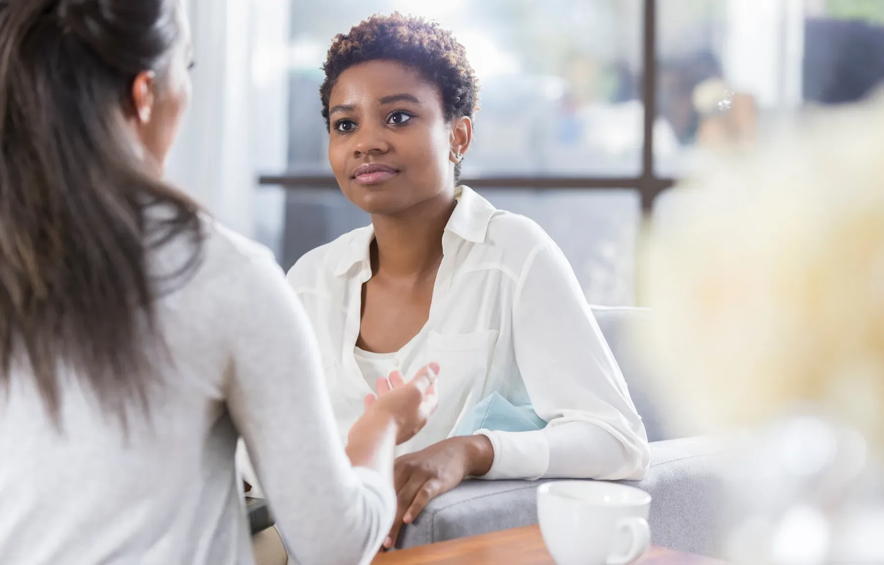 A Black female therapist with a short curly natural hairstyle and a white blouse listens with a calm, thoughtful expression w