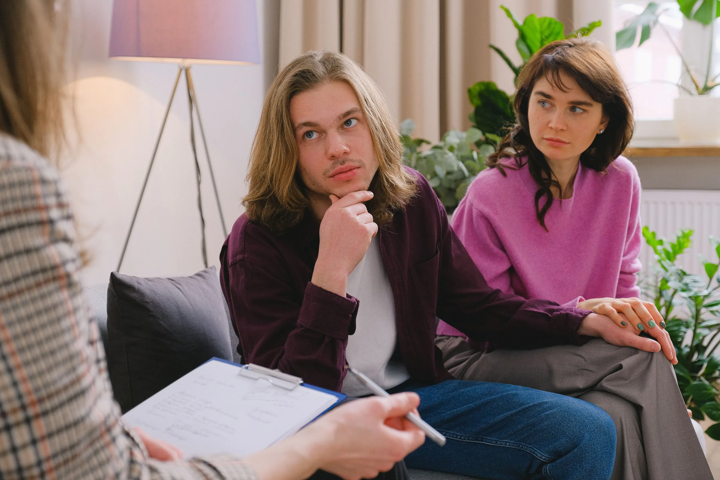 Two people listen attentively during a therapy session in a modern office with plants and soft lighting.